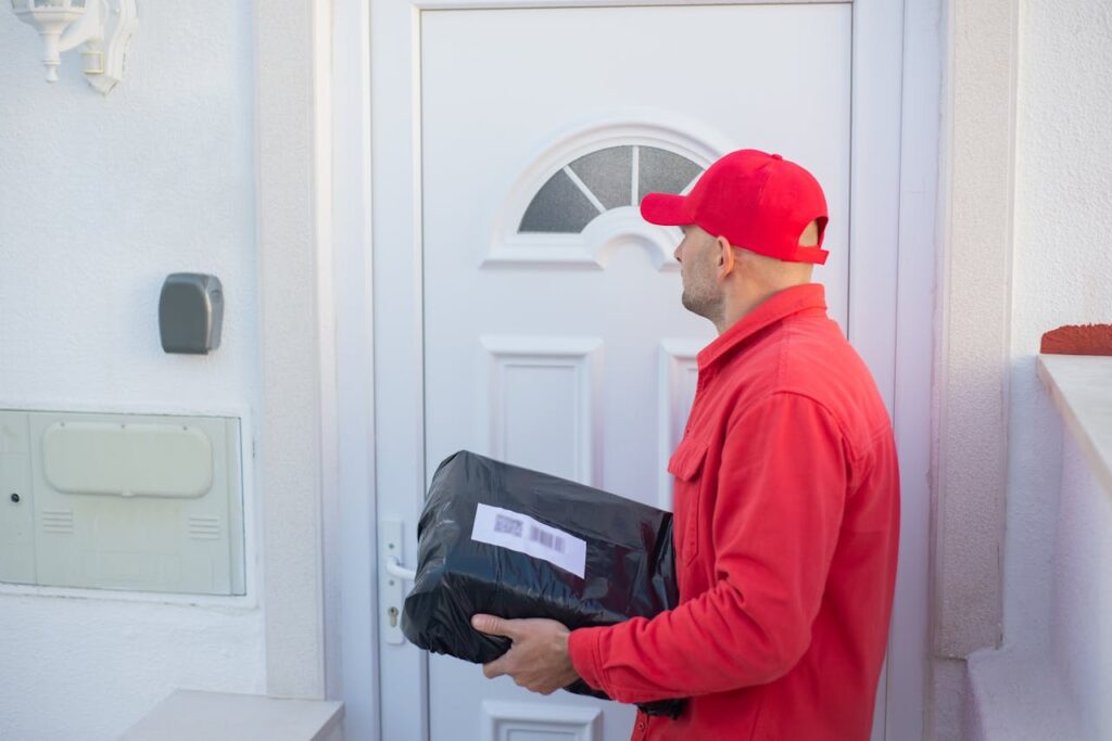 pexels-photo-6667679 A delivery man in a red uniform holding a package at a residential door.